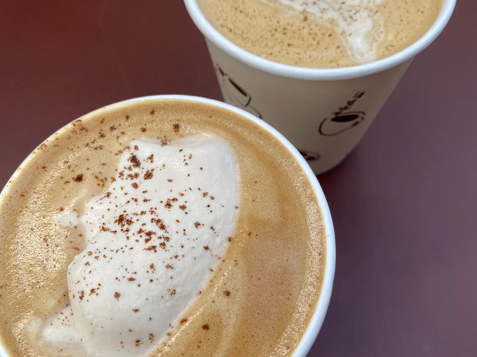 Two lattes with foam and a dusting of cinnamon on a café table