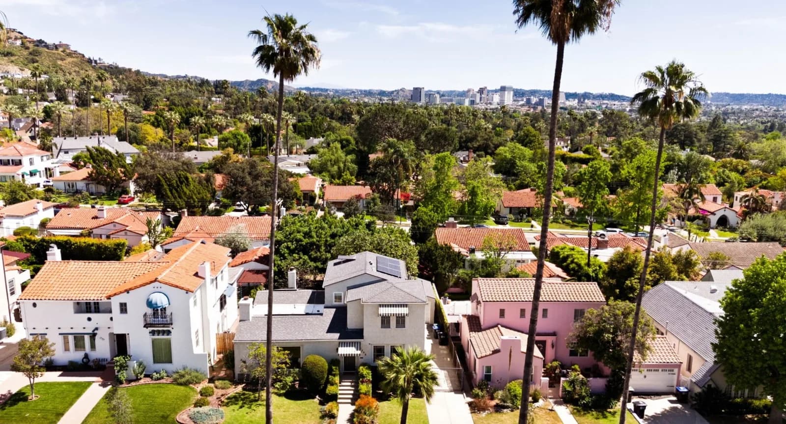 Aerial view of Spanish-style homes and palms on a Glendale street, with the downtown skyline and hills behind