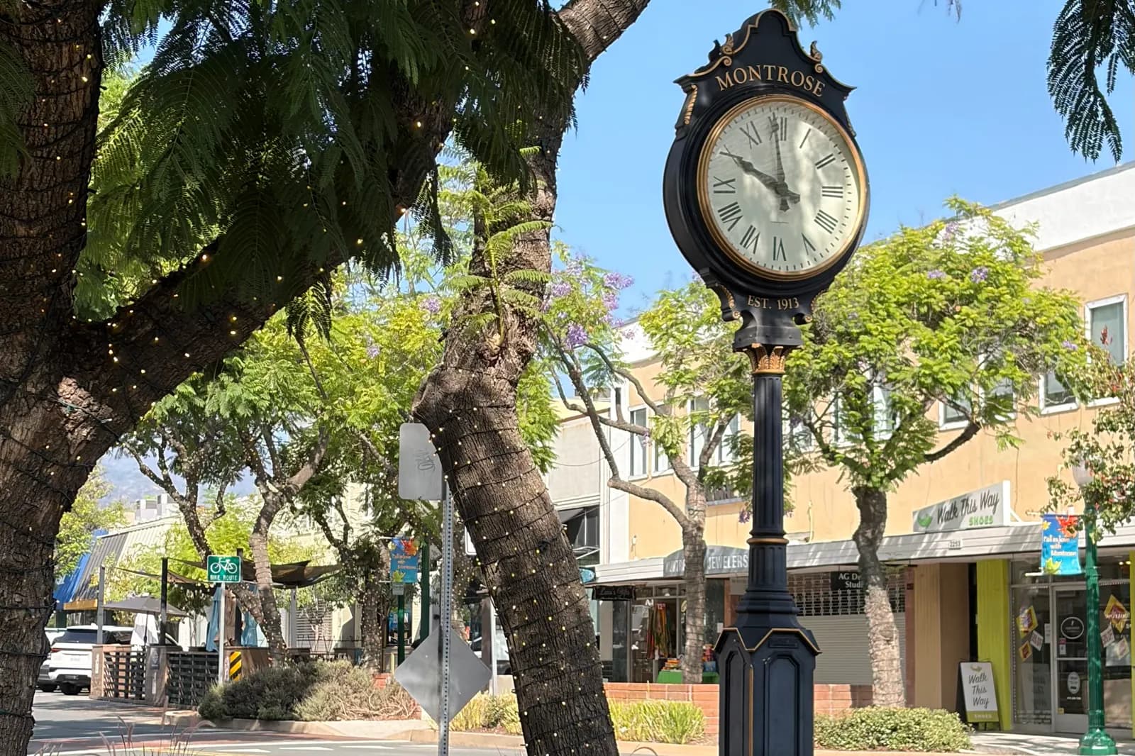 The Montrose street clock on Honolulu Avenue under light-wrapped trees, with the shops behind it