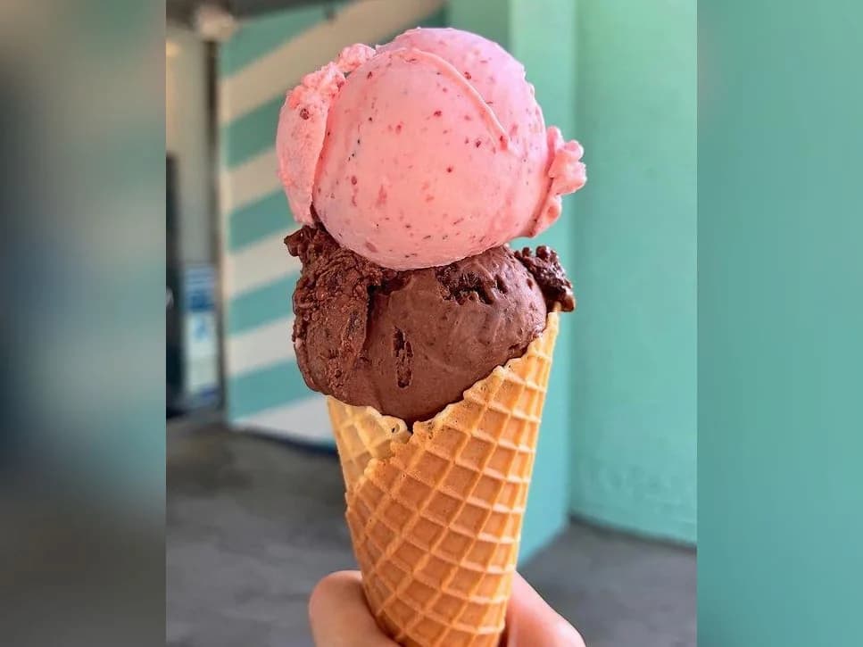 A waffle cone with a scoop of strawberry and a scoop of chocolate ice cream from Moo Moo Mia