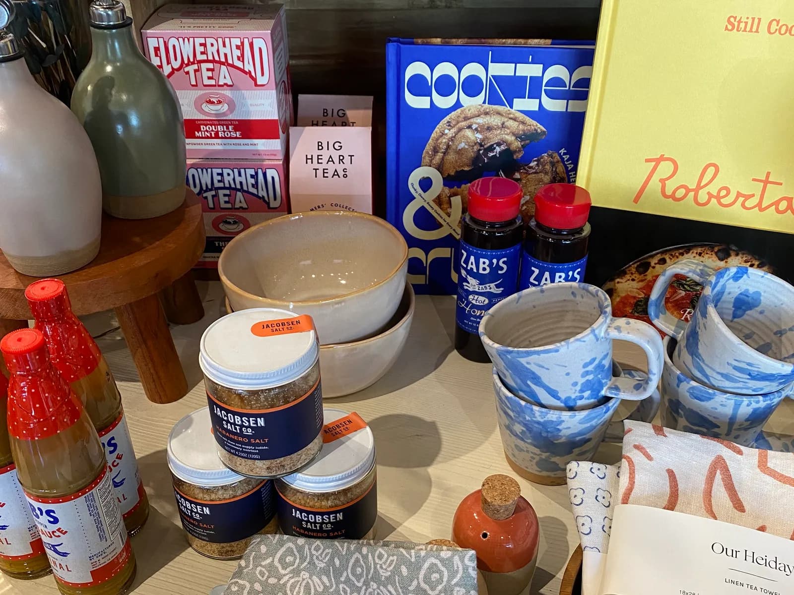 A gift shop table of tea tins, cookbooks, splatter-glazed mugs, salt jars and linen tea towels