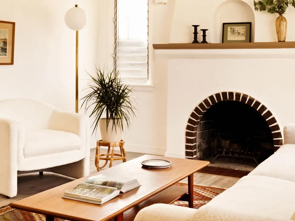 Staged living room with a white plaster fireplace, brick arch and a teak coffee table on a kilim rug